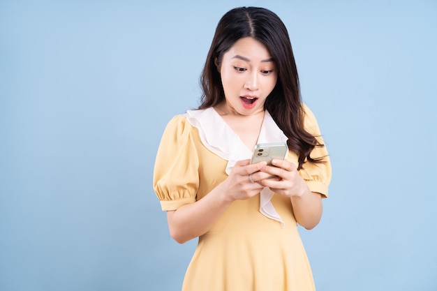 Mulher jovem e bonita asiática usando smartphone em fundo azul