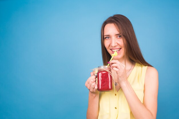 Mulher jovem e bonita bebe smoothie de morango em azul. Conceito de bebidas orgânicas saudáveis. Pessoas de dieta.