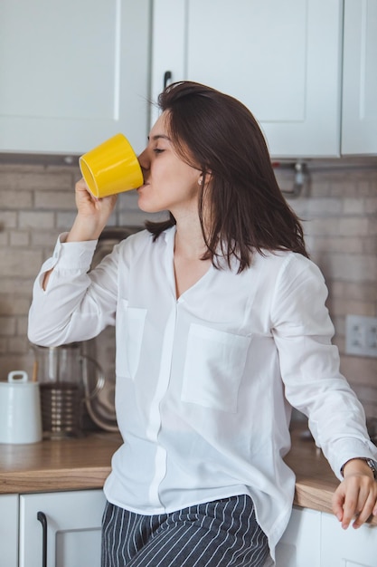 Mulher jovem e bonita bebendo chá da caneca amarela na cozinha. doce lar