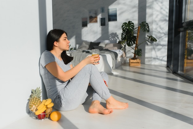 Mulher jovem e bonita bebendo suco fresco no quarto