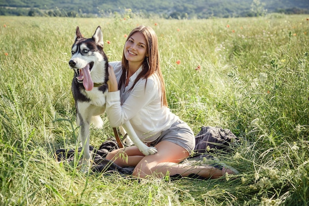 Mulher jovem e bonita brincando com um cachorro husky engraçado ao ar livre no parque