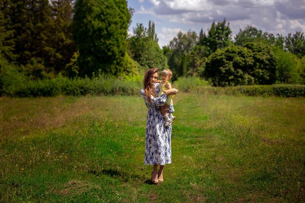 Mulher jovem e bonita caminha carregando a filha no jardim em um dia quente de verão