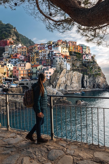 Mulher jovem e bonita caminhando ao longo do passeio marítimo de Manarola olhando para a deslumbrante vista panorâmica da vila de Manarola em Cinque Terre