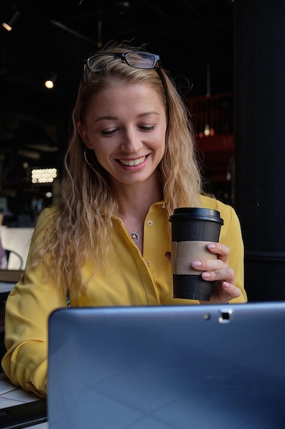 Mulher jovem e bonita cauasiana sentada em uma cafeteria digitando no teclado de um laptop