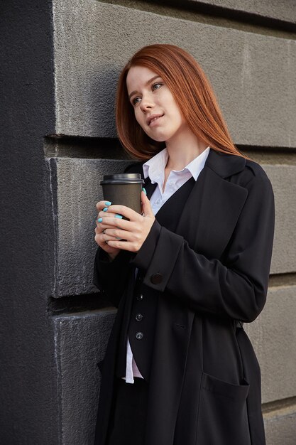 Mulher jovem e bonita caucasiana com casaco bege elegante, bebendo café ao ar livre