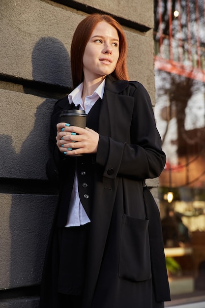 Mulher jovem e bonita caucasiana com elegante casaco bege tomando café ao ar livre