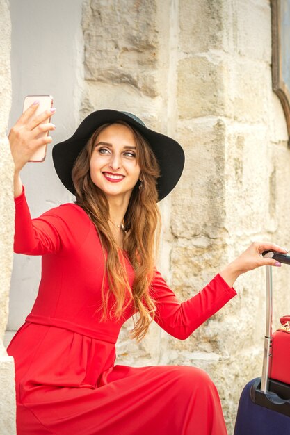 Mulher jovem e bonita caucasiana de chapéu preto, olhando no smartphone sorrindo e sentado na escada ao ar livre da porta.