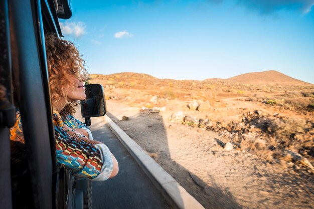 Mulher jovem e bonita caucasiana viajando com um carro preto off-road e olhando para fora da paisagem