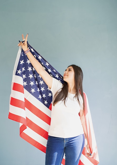 Mulher jovem e bonita com a bandeira americana sobre fundo azul