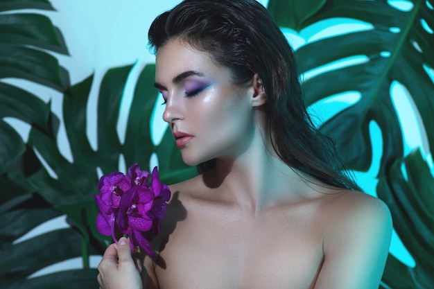 Mulher jovem e bonita com a pele lisa perfeita está segurando flores da orquídea