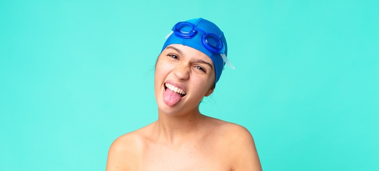 Foto mulher jovem e bonita com atitude alegre e rebelde, brincando e mostrando a língua com óculos de natação