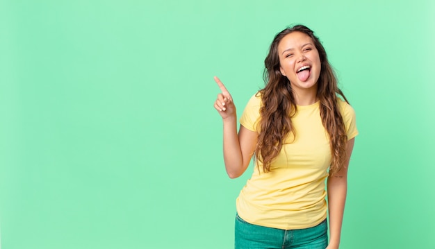 Mulher jovem e bonita com atitude alegre e rebelde, brincando e mostrando a língua e apontando para o espaço da cópia