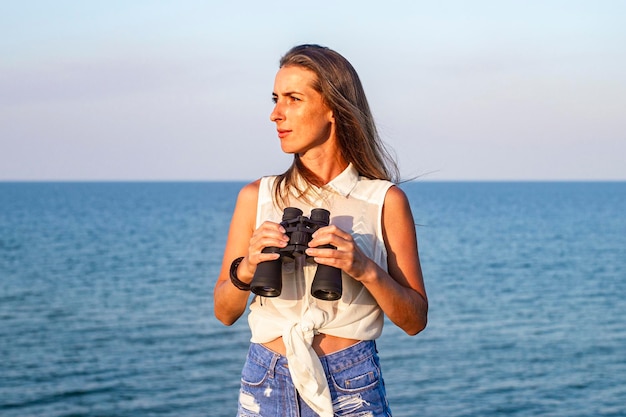 Mulher jovem e bonita com binóculos no penhasco olha para o mar