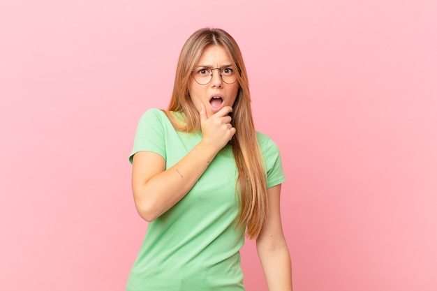 Mulher jovem e bonita com boca e olhos bem abertos e mão no queixo