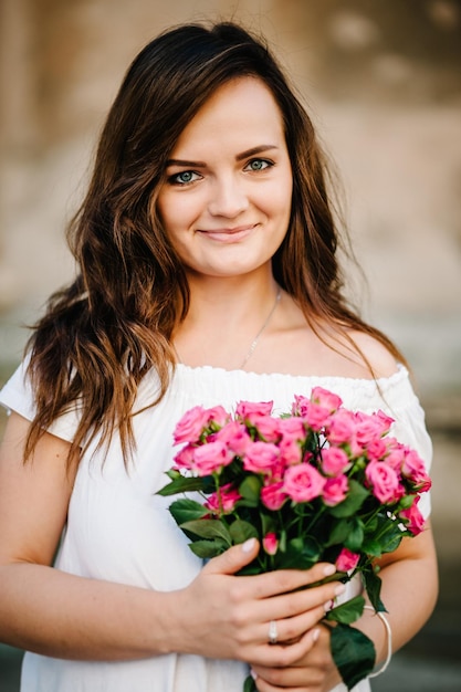 Mulher jovem e bonita com buquê de flores de primavera na rua da cidade. Garota feliz sorrindo e segurando flores rosas cor de rosa ao ar livre. Retrato de primavera de muito mulher.