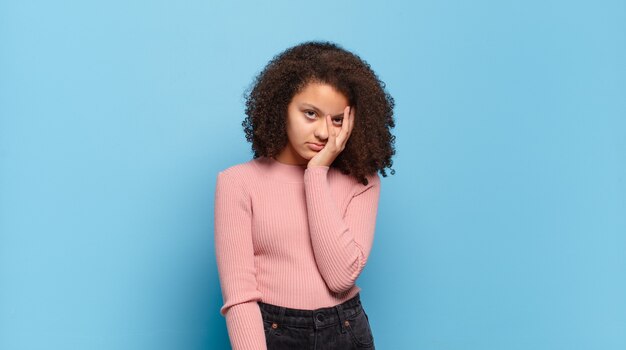 Mulher jovem e bonita com cabelo afro e suéter rosa posando na parede azul