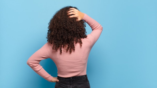 Mulher jovem e bonita com cabelo afro e suéter rosa posando na parede azul