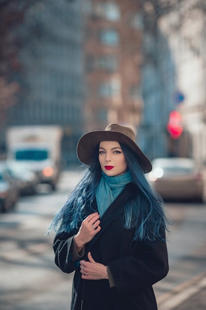 Mulher jovem e bonita com cabelo azul em um belo casaco preto, jeans e chapéu.