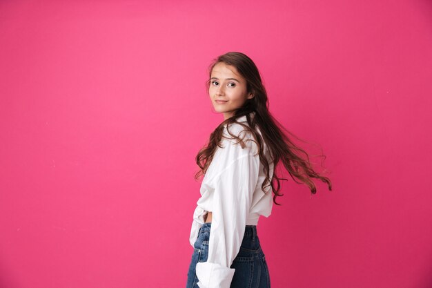 Mulher jovem e bonita com cabelo comprido encaracolado em pé e olhando para a frente, isolado na parede rosa