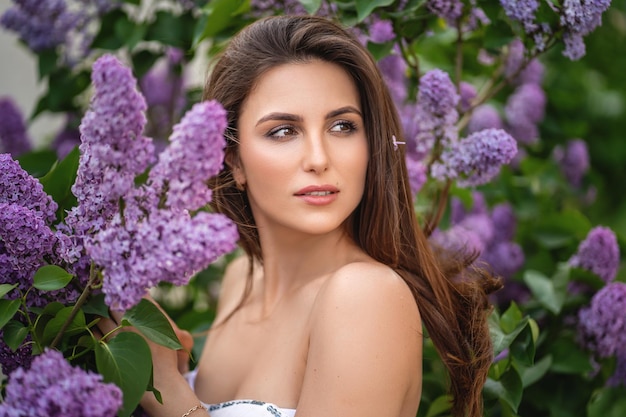 Mulher jovem e bonita com cabelo comprido por um lilás florescendo