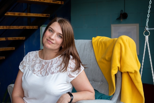 Mulher jovem e bonita com cabelo comprido ruivo em uma blusa branca, sentada em uma cadeira em um café sozinha, esperando seu pedido.