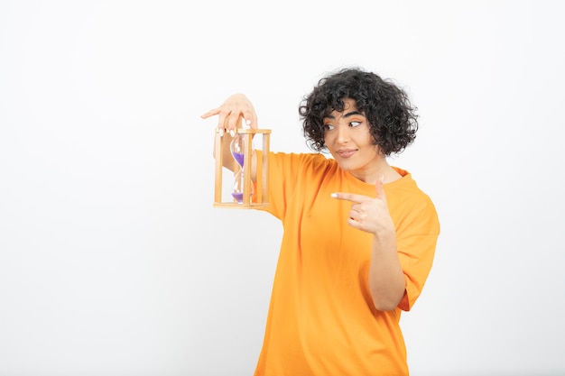 Mulher jovem e bonita com cabelo encaracolado, apontando para a ampulheta.