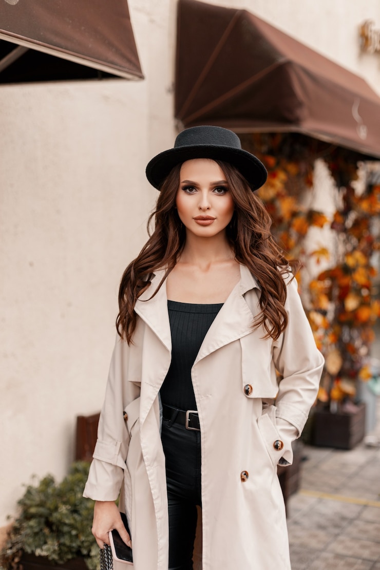 Foto mulher jovem e bonita com cabelo encaracolado com um chapéu da moda com um clássico casaco cinza andando pela cidade em um dia de outono