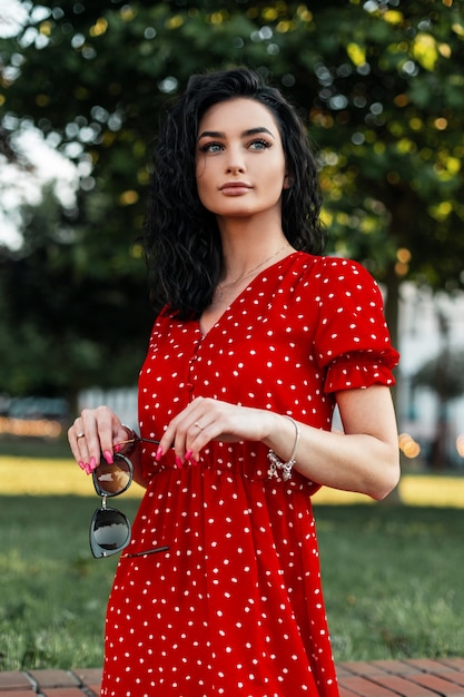 Mulher jovem e bonita com cabelo encaracolado com um vestido vermelho da moda caminhando no parque