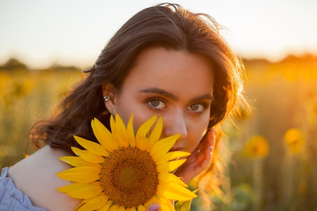 Mulher jovem e bonita com cabelo encaracolado escuro em um campo de girassol Modelo em um elegante vestido azul Summer Warmly