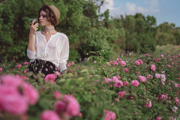 Mulher jovem e bonita com cabelo encaracolado posando perto de rosas em um jardim O conceito de publicidade de perfume