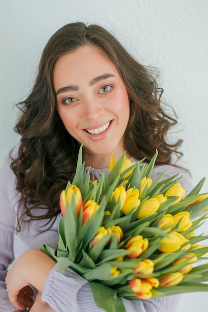 Mulher jovem e bonita com cabelo encaracolado segura um buquê de tulipas.