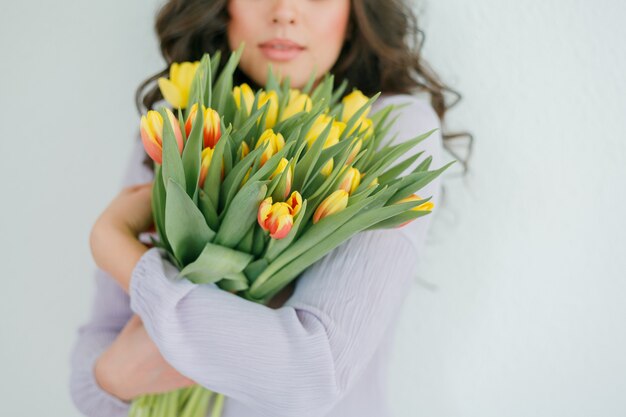 Mulher jovem e bonita com cabelo encaracolado segura um buquê de tulipas.