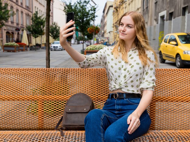 Mulher jovem e bonita com cabelo loiro tirando selfie na cidade