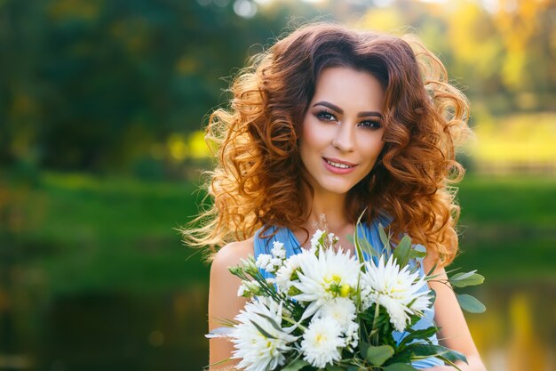 Mulher jovem e bonita com cabelo longo cacheado posando com buquê