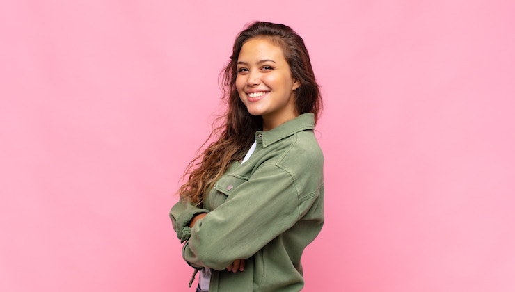 Foto mulher jovem e bonita com camisa aberta jeans verde posando na parede rosa