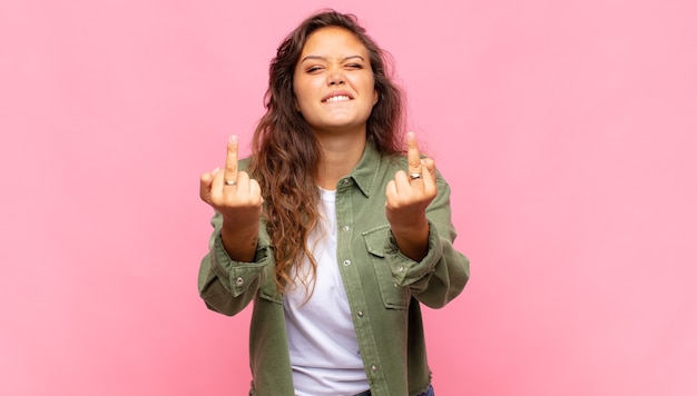 Foto mulher jovem e bonita com camisa aberta jeans verde posando na parede rosa