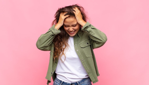 Mulher jovem e bonita com camisa aberta jeans verde posando na parede rosa