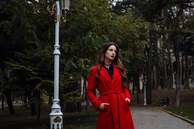 Mulher jovem e bonita com casaco vermelho está aproveitando o parque outono. Um passeio agradável no fundo do parque