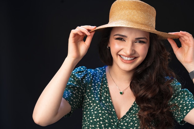 Mulher jovem e bonita com chapéu de palha posando contra um fundo preto