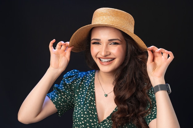 Mulher jovem e bonita com chapéu de palha posando contra um fundo preto