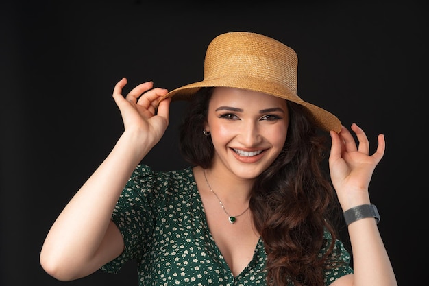 Mulher jovem e bonita com chapéu de palha posando contra um fundo preto