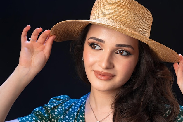 Mulher jovem e bonita com chapéu de palha posando contra um fundo preto