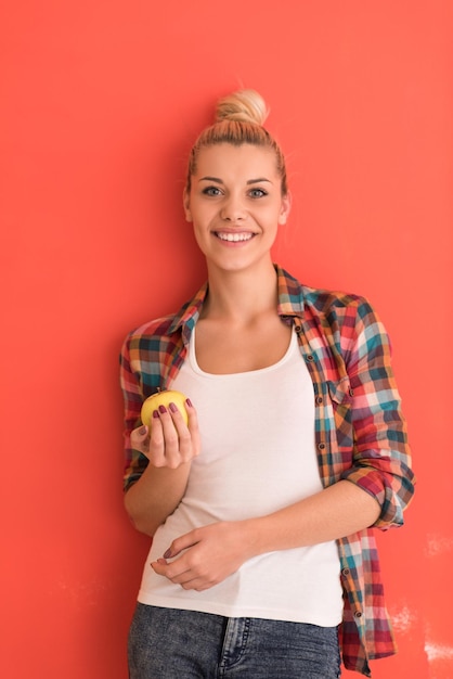 mulher jovem e bonita com coque de cabelo joga com maçã sobre fundo de cor com copyspace expressando emoções diferentes