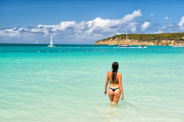 Foto mulher jovem e bonita com corpo bonito em maiô em pé na água do oceano dia ensolarado ao ar livre