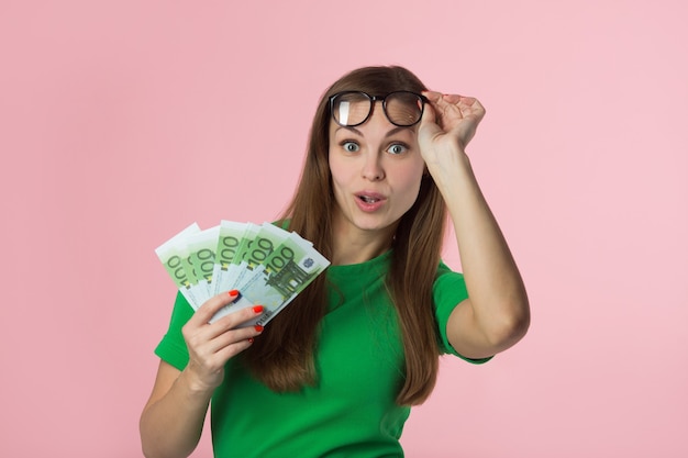 Mulher jovem e bonita com dinheiro do euro em fundo rosa