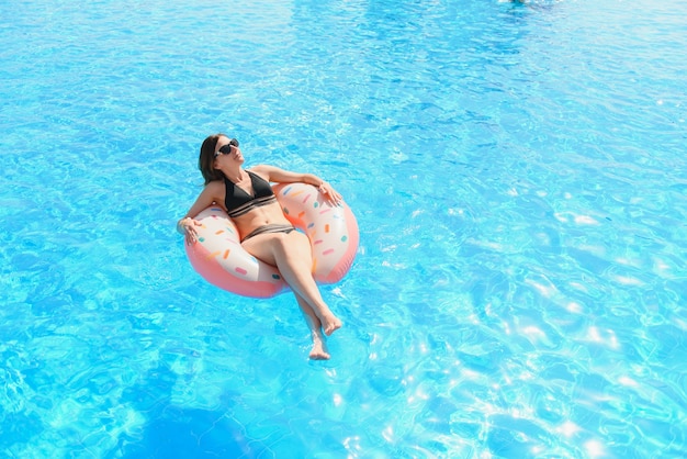 Mulher jovem e bonita com donut inflável na piscina azul