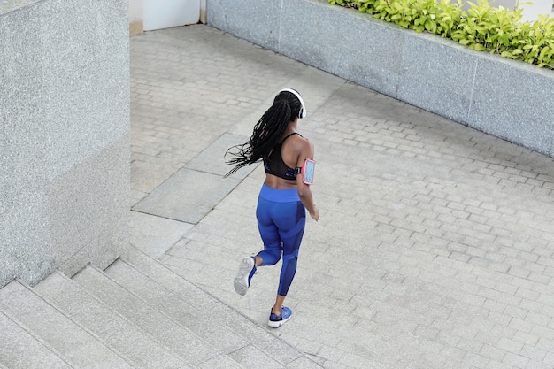 Mulher jovem e bonita com dreadlocks correndo na rua, vista de trás