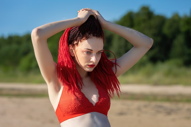 Mulher jovem e bonita com dreadlocks escarlates e maiô vermelho, curtindo a natureza.