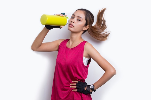 Mulher jovem e bonita com esportes asiáticos bebendo água após o treino em fundo branco