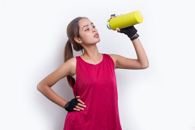 Mulher jovem e bonita com esportes asiáticos bebendo água após o treino em fundo branco